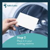 A hand holding a SaltyLama laundry detergent strip in front of a washing machine. SaltyLama laundry detergent strips can be placed in any washing machine.